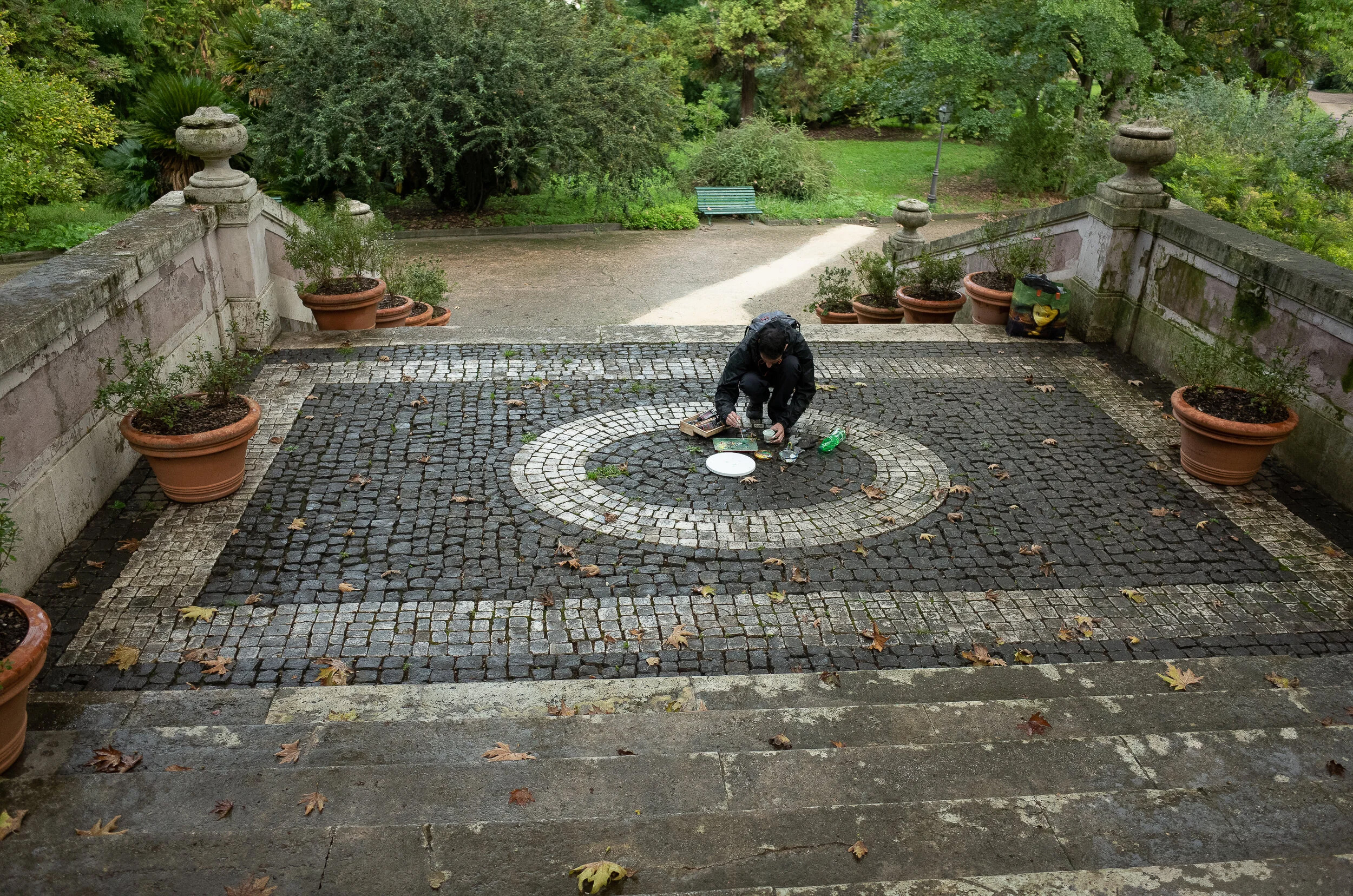 Artist crouched on cobblestone mosaic courtyard in the rain