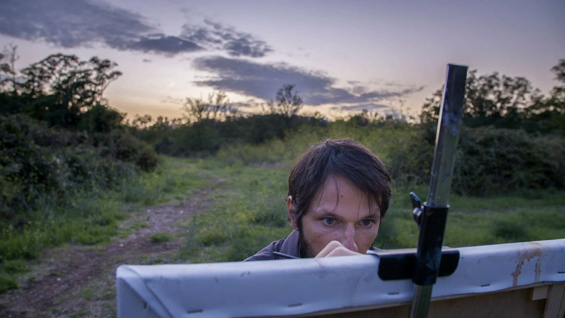 Artist peeking over canvas at dusk in Tor Marancia field