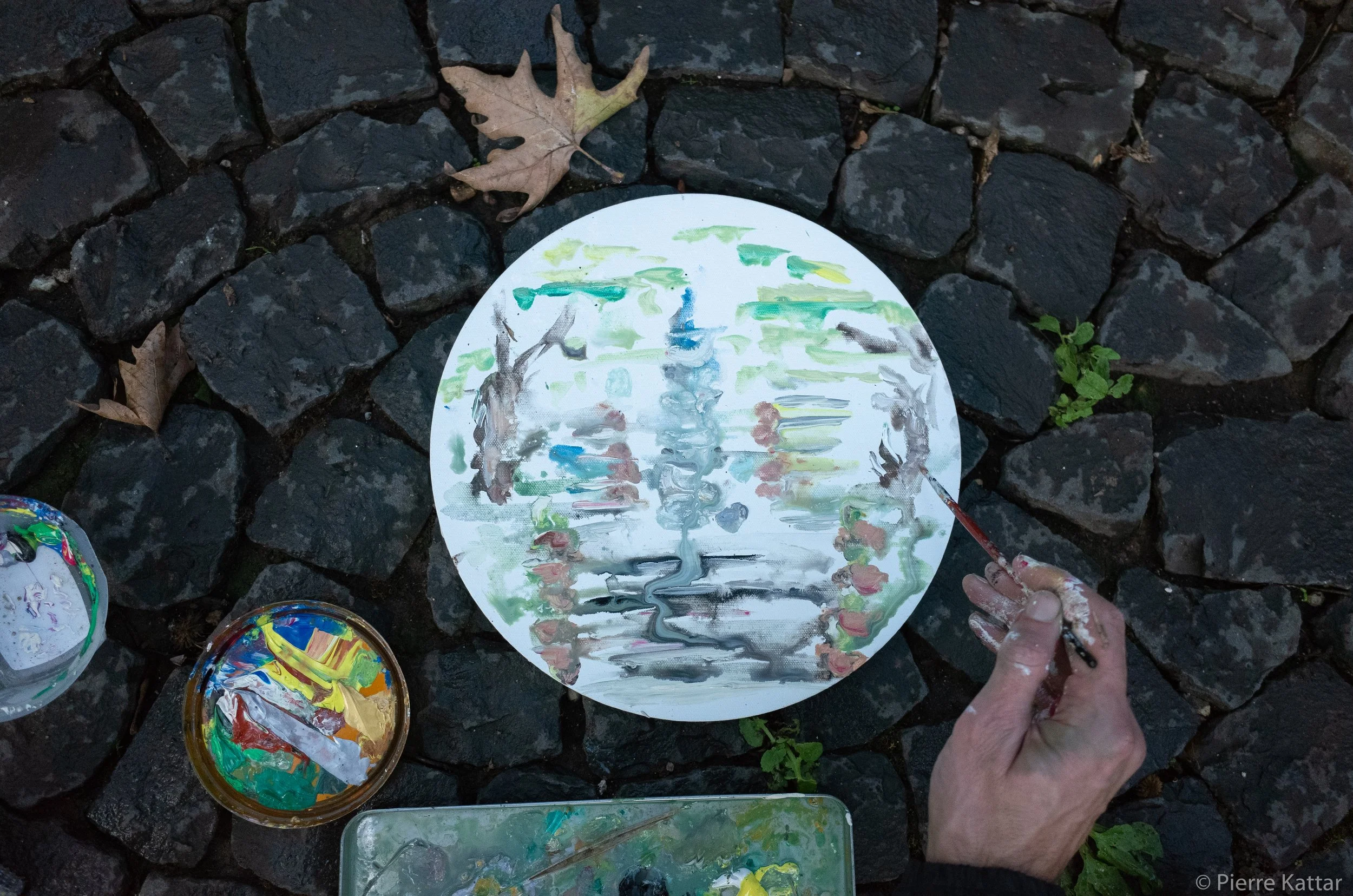 Circular canvas painting on cobblestones with artist's hand and paint palette