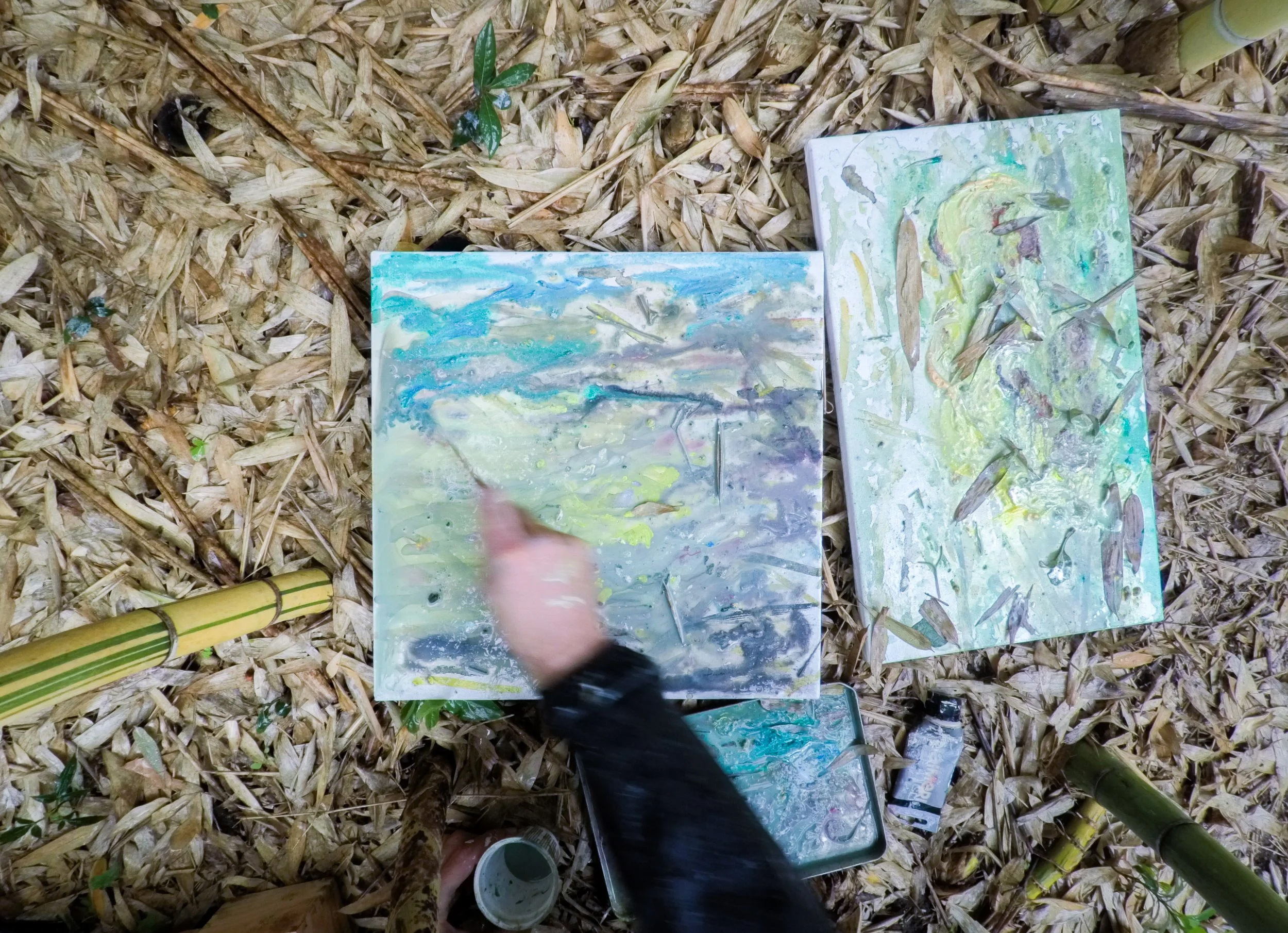 Artist painting two canvases on bamboo leaves